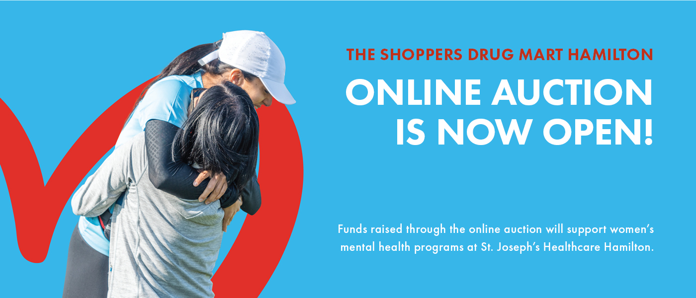 The image has a bright blue background with a red heart outline in the bottom-left corner. There are two women hugging in front of the heart shape. The following text appears on the left side of the image: The Shoppers Drug Mart Hamilton Online Auction is Now Open! Funds raised will support women's mental health programs and services at St. Joseph's Healthcare Hamilton.